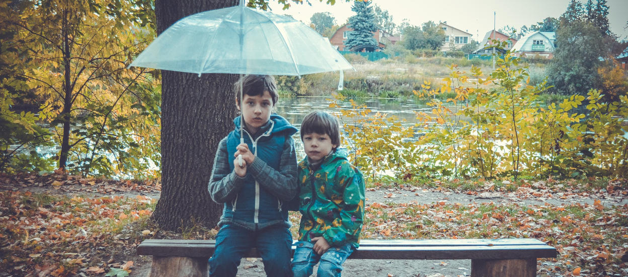 Children in the rain at autumn, holding an umbrella