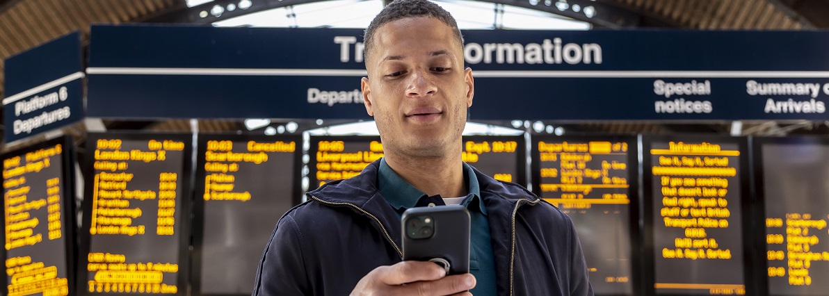 Man checking his phone in front of train departure board 