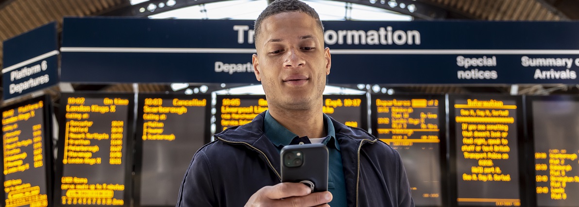 Man checking his phone in front of train departure board