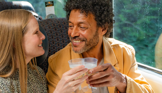 Couple sat on the train clinking their prosecco glasses together in celebration