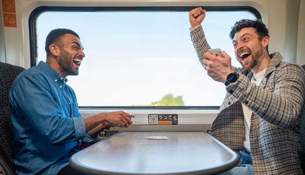 Two friends on train playing cards and celebrating 