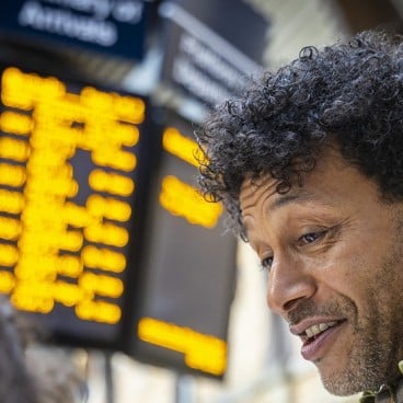 man in front of departures board at train station.