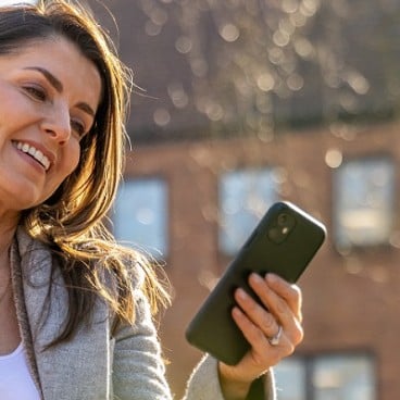 woman sat down in a park smiling at her phone